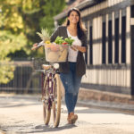 Frau schiebt Fahrrad mit Fahrradkorb voller Obst und Gemüse