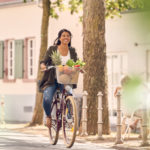 Frau auf Fahrrad mit Fahrradkorb voller Obst und Gemüse