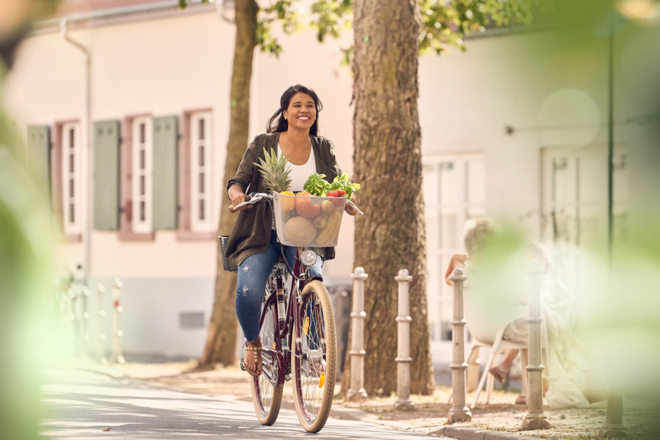 Frau auf Fahrrad mit Fahrradkorb voller Obst und Gemüse