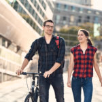 Frau und Mann laufen über Campus, Mann schiebt Fahrrad