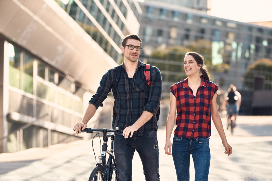 Frau und Mann laufen über Campus, Mann schiebt Fahrrad