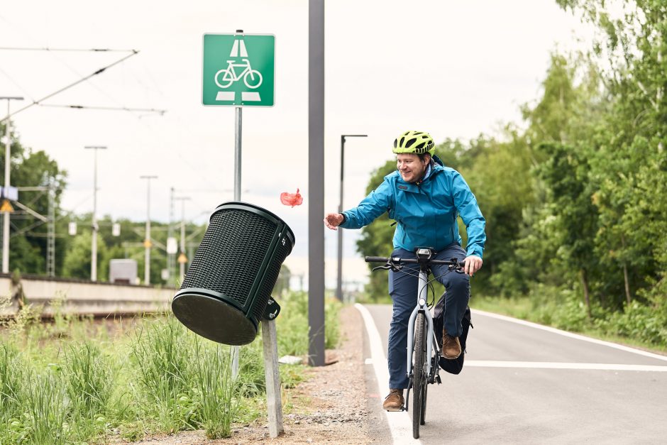 Radfahrer auf Radschnellweg wirft Müll in schräg angebrachten Abfalleimer