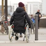 Rollstuhlfahrerin fährt über abgesenkten Bordstein