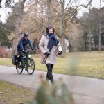 Im Park unterwegs: Frau zu Fuß und Mann auf dem Fahrrad