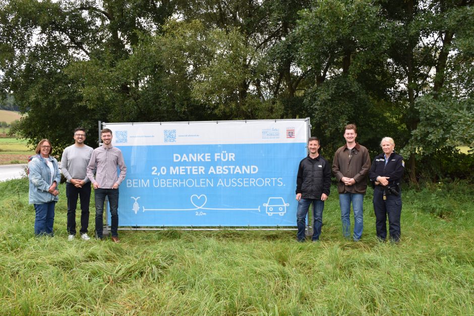 Ein Banner zum Radverkehr "Zwei Meter Abstand" mit Personen links und rechts davon