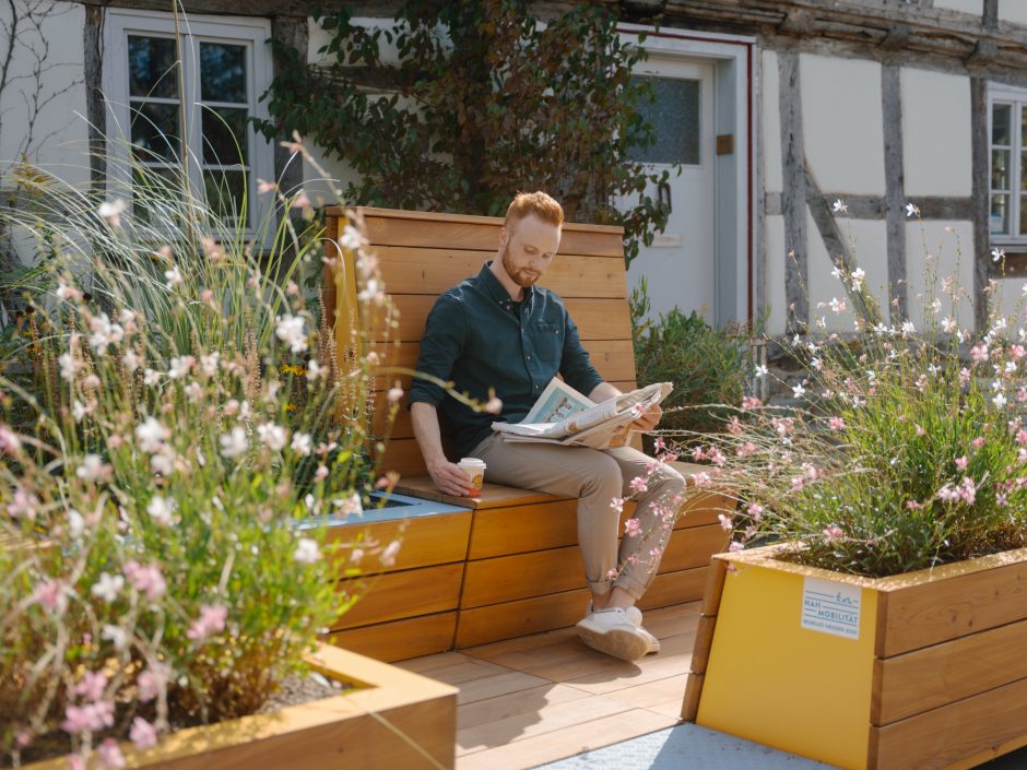 Person mit Zeitung und Getränk auf Sitzbank